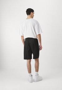 Camiseta blanca oversized, pantalones cortos deportivos negros y zapatillas blancas. Materiales ligeros y casuales con un ajuste relajado. Diseño minimalista.