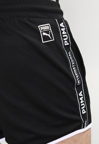Shorts de sport noirs en tissu respirant, avec des accents blancs et une marque Puma sur les côtés et la ceinture.