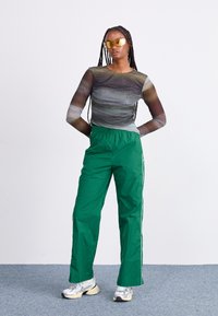 Διαφανής μπλούζα με μακριά μανίκια και στροβ�ιλιζόμενα καφέ και γκρίζα μοτίβα; πράσινα αθλητικά παντελόνια με λευκές ρίγες στο πλάι; ασημένια αθλητικά παπούτσια; κίτρινες γυαλιά ηλίου.