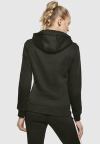 Hoodie noir avec une poche avant et un capuchon réglable avec cordon, présentant des poignets et un ourlet côtelés. Tissu lisse avec une coupe ajustée.
