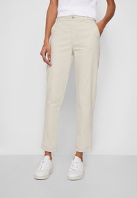 Beiga chinos gjorda av bomull, med rak benmodell, framfickor och uppvikta ärmslut, i kombination med vita sneakers.