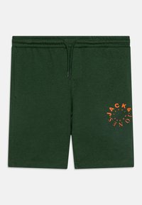 Shorts en coton verts avec une taille élastique et un cordon de serrage. Présente un logo circulaire orange sur le côté gauche. Texture lisse.