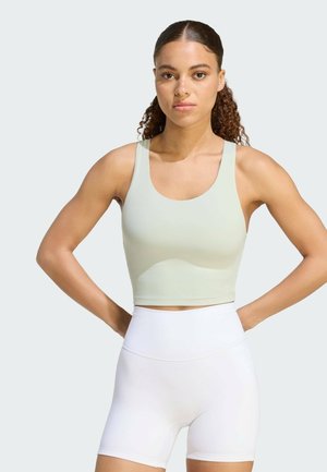 Kvinde med krøllet hår iført en lysegrøn sport crop top og hvide atletikshorts med høj talje, stående med hænderne på hofterne.