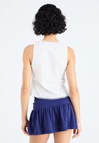 Top bianco senza maniche con motivo ad occhiello e bordo scallop, abbinato a una gonna navy blu a campana realizzata in morbido jersey.