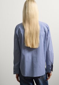 Camisa de cuadros azul y blanca de manga larga con puños de botón, hecha de una tela ligera, combinada con jeans de mezclilla oscura.