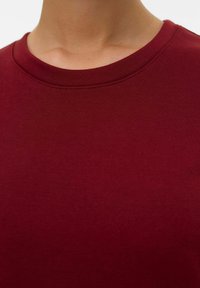 Sudadera de cuello redondo burdeos, fabricada en suave mezcla de algodón, de mangas cortas, con textura lisa y un detalle de costura mínima cerca del cuello.