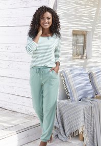 Mint zaļas ikdienas bikses ar auklu jostu, apvienotas ar gaiši zilu un baltu svītrainu garām piedurknēm kreklu. Koksnes fons ar spilveniem.