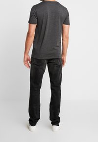 Camiseta gris de manga corta combinada con jeans negros. La camiseta tiene un cuello redondo, mientras que los jeans cuentan con bolsillos traseros y un diseño de pierna recta.