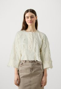 Light beige cropped blouse with frayed texture, round neckline, and three-quarter sleeves, paired with a high-waisted beige denim skirt.