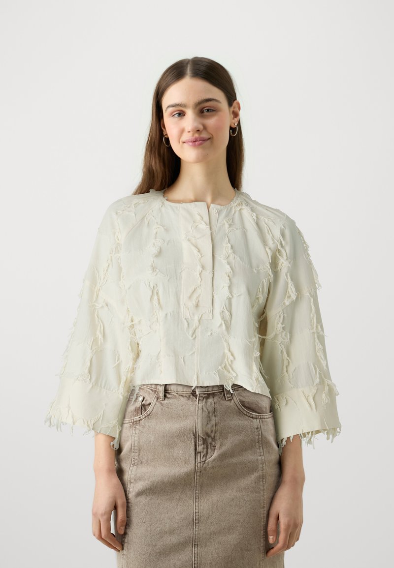 Light beige cropped blouse with frayed texture, round neckline, and three-quarter sleeves, paired with a high-waisted beige denim skirt.