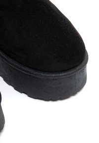 Juodos suede aulinukų iki kulkšnies su apvaliu pirštu ir storu, tekstūruotu guminio pado. Lygus paviršius be akivaizdaus furnitūros ar raštų.