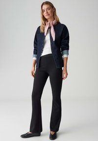 Dunkelblaue Jeans-Hemdjacke mit hellblauen Manschetten, weißem Oberteil, schwarzen Schlaghosen und einem rosa Schal, der um den Hals gebunden ist. Schwarze Ballerinas.