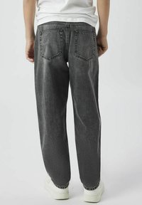 Grå bomullsdenimbyxor med avslappnad passform, synlig sömnad, två bakfickor och elastiska muddar vid fållen, tillsammans med vita sneakers.