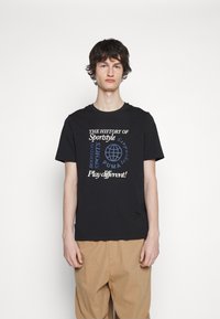 Zwarte katoenen T-shirt met grafische tekst waaronder "DE GESCHIEDENIS VAN" en "Speel anders!" in wit en blauw. Casual pasvorm, korte mouwen.