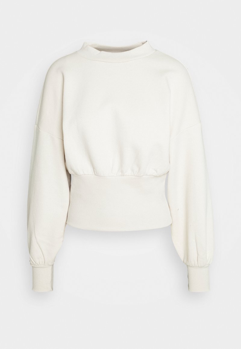 Sweat-shirt court à manches longues de couleur crème avec un col haut, une taille froncée et des poignets côtelés sur un fond uni.