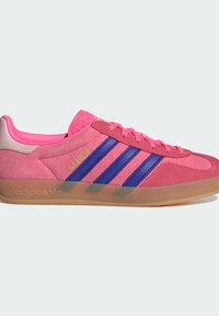 Zapatilla de ante rosa con puntera texturizada, tres rayas azules a un lado y una suela de goma transparente. Presenta cordones rosas y una marca.