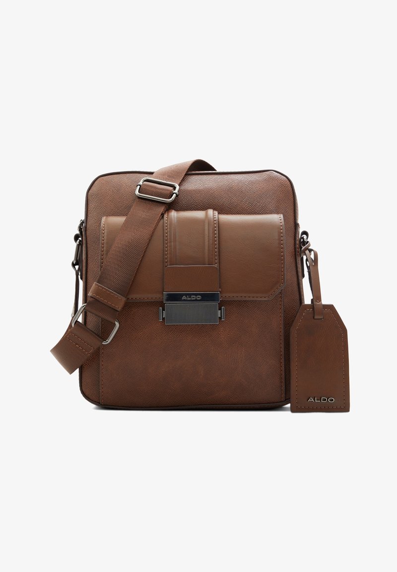 Hnědá kožená crossbody taška s texturovaným povrchem, vybavená magnetickým překrytím, nastavitelným popruhem a visačkou na zavazadla.