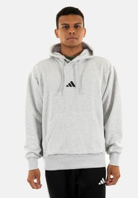 Felpa grigia con cappuccio realizzata in tessuto morbido, con tasca a marsupio frontale e logo nero sul petto. Polsini e orlo a coste.