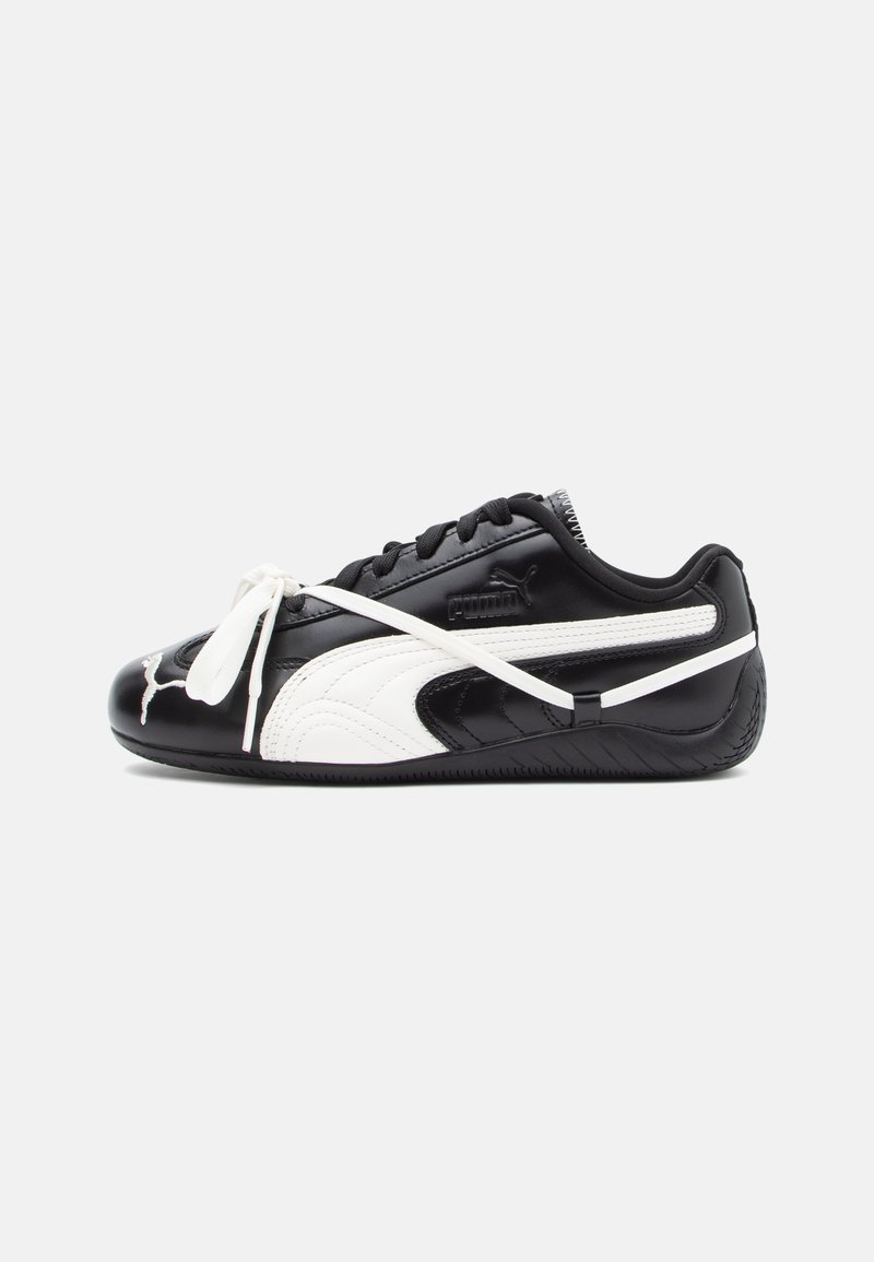 Tenisi alb-negru cu un finisaj din piele lucioasă, vârf rotunjit, talpă din cauciuc proeminentă și șireturi subțiri albe. Logo-ul PUMA este vizibil.