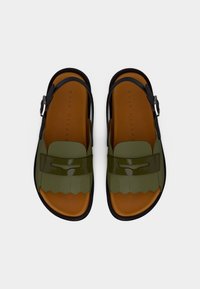 Πράσινα και μαύρα σανδάλια με υφασμάτινο λουράκι, γυαλιστερές λεπτομέρειες και κυματοειδές σχέδιο μπροστά. Καφέ εσωτερική σόλα με λουράκι και αγκράφα.