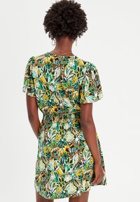 Robe florale à manches courtes, présentant un motif vert, jaune et marron. Taille élastiquée et détail de tissu légèrement froncé.