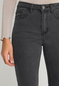 Jeans negros de tiro alto con una textura suave, que cuentan con detalles de costura y bolsillos delanteros, combinados con una blusa de manga larga ligera.