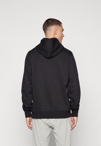 Felpa nera con cappuccio, caratterizzata da un finish testurizzato, cappuccio grande, polsini e orlo a costine, mostrata da dietro. Vestibilità casual e design semplice.