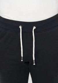 Primo piano di pantaloni della tuta neri con coulisse bianche che pendono dalla vita a coste sopra un top bianco.