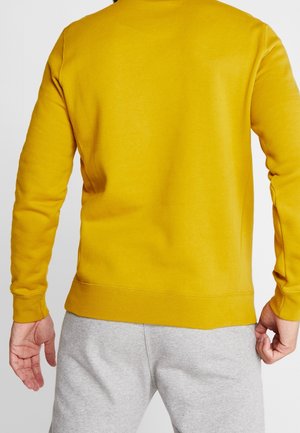Sudadera amarilla con cuello redondo y puños acanalados, combinada con pantalones de chándal grises. Textura suave, diseño ajustado y color sólido.