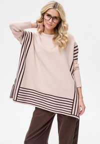 Lichtbeige oversized trui met donkerbruine gestreepte accenten aan de zoom en mouwen, voorzien van een ronde halslijn en zijsplitten.