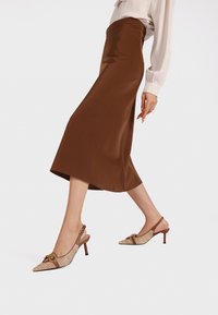 Gonna midi in satin marrone con una texture liscia, abbinata a décolleté beige con un motivo intrecciato e tacco basso.