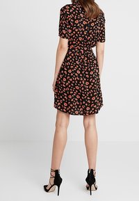 Kortärmad, svart klänning med ett rött leopardmönster, åtsittande midja och flödande kjol, i kombination med svarta högklackade sandaler.