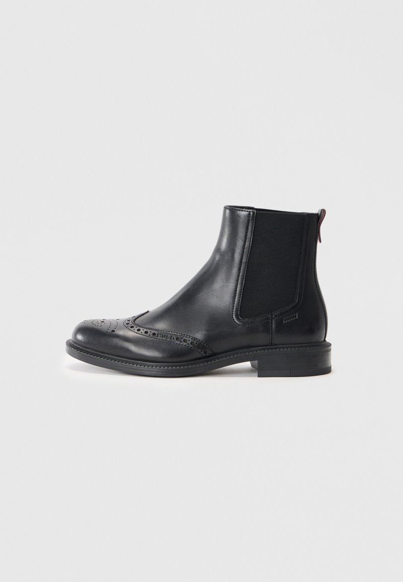 Stivale Chelsea in pelle nera con dettagli a brogue, pannelli laterali elastici e una linguetta sul retro. Tacco basso e design elegante.