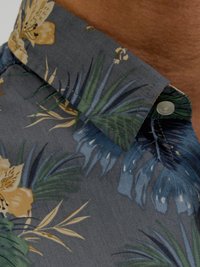 Chemise à manches courtes florale en tissu gris avec des fleurs jaunes, des feuilles vertes et bleues. Col à boutons. Matériau léger et texturé.