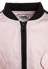 Rosa bomberjacka med en svart ribbad krage och dragkedja, med sidofickor och en slät, lätt tygtextur.