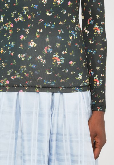 Top cu model floral, cu mânecă lungă, dintr-un material închis, combinat cu o fustă stratificată de culoare albastră deschisă. Topul are o textură ribbed și o margine contrastantă.