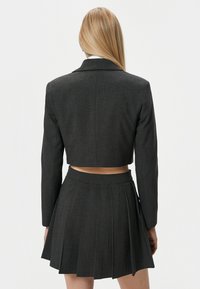 Grijze, op maat gemaakte cropped blazer gecombineerd met een bijpassende geplooide rok. Beide hebben een gladde textuur en een gestructureerd ontwerp.