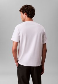 Bijela pamučna majica kratkih rukava, ravnog kroja i okruglog izreza. Minimalistički dizajn bez uzoraka ili vidljivih oznaka brenda.