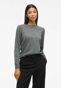 Pull gris à manches longues en tissu doux, avec un col rond et des poignets ajustés, associé à un pantalon noir ajusté.