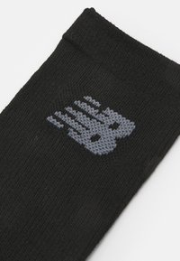 Calcetín negro hecho de tejido de punto con un logotipo "NB" en gris. El diseño incluye un puño acanalado en la parte superior para mayor comodidad y ajuste.