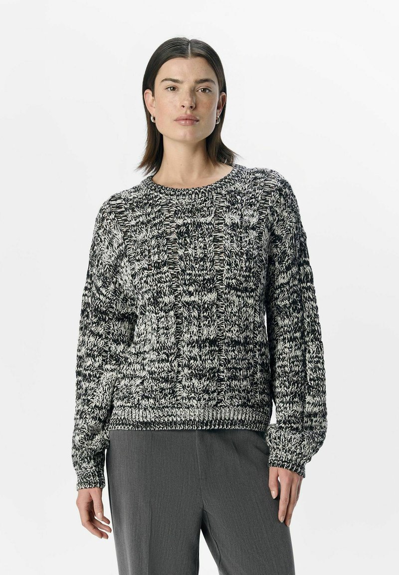 Maglione lavorato a maglia in bianco e nero con un motivo testurizzato, scollatura rotonda e polsini a coste. Indossato con pantaloni grigi, caratterizzati da una vestibilità rilassata.