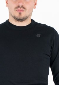 Maglietta a maniche lunghe nera a costine con scollatura rotonda e tessuto Texturizzato. Presenta un piccolo logo nero sul petto.