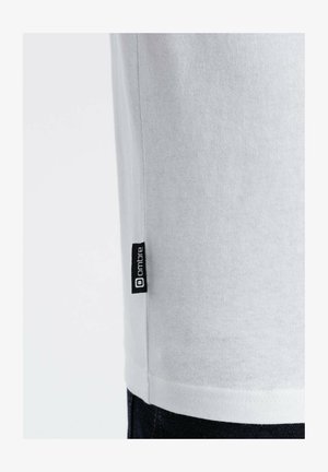 Witte katoenen T-shirt met korte mouwen, voorzien van een zwart merklabel op de zijnaad. Vloeiende textuur en eenvoudig ontwerp.