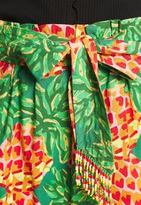 Kolorowa tkanina z zielonymi liśćmi i wzorami kwiatowymi, z muszką w talii i koralikowymi frędzlami.