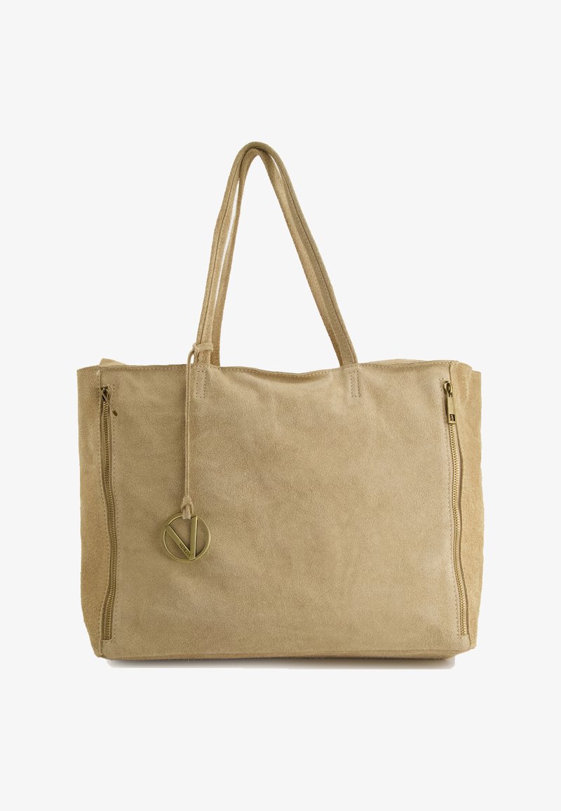Beige suede tote bag with dual side zippers and a circular metal charm. Features two long, flat handles for easy carrying.