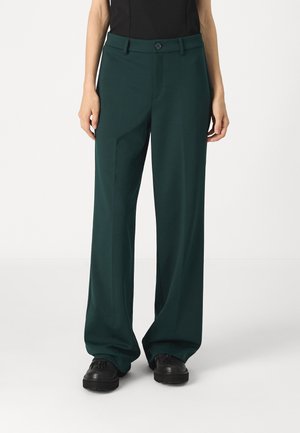 Pantaloni a gamba larga verde scuro con una texture liscia, dotati di cintura, chiusura con bottone e tasche laterali, abbinati a scarpe nere.