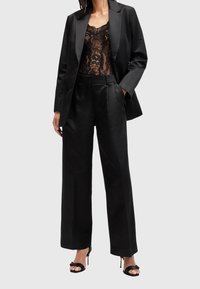 Černý dobře sestřižený blazer přes černý krajkový body, doplněný o černé kalhoty s vysokým pasem a černé sandály na podpatku, hladké textury a minimalistický design.