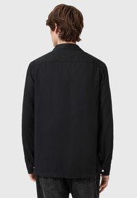 Sort langærmet skjorte med spids krave og knapmanchetter, der har en glat tekstur og en lige kant.