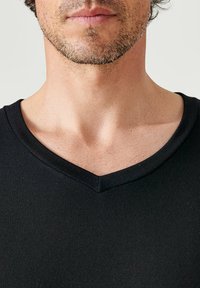 Black V-neck shirt featuring a ribbed texture and a short sleeve design. The neckline has a mid-depth V shape with clean edges.