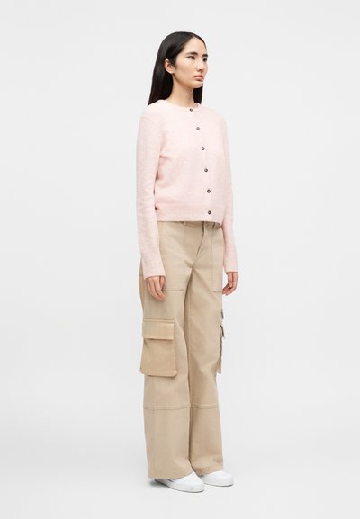 Ανοιχτό ροζ, μακρυμάνικη ζακέτα με στρογγυλή λαιμόκοψη και κουμπιά στο μπροστινό μέρος, συν δυασμένη με μπεζ παντελόνι cargo με πολλαπλές τσέπες και φαρδιά εφαρμογή.